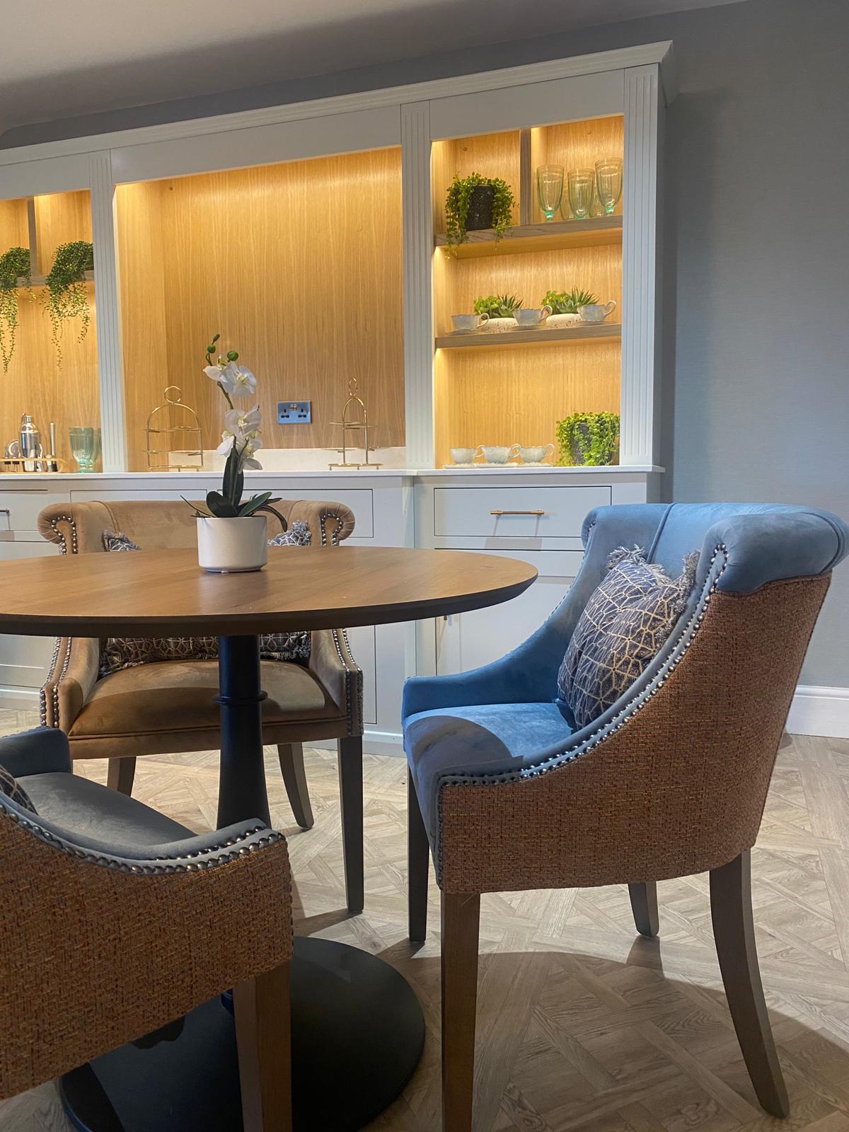 The café seating area at Meadowbrook Manor care home showing comfortable upholstered chairs around a round dining table with fresh orchid centrepiece