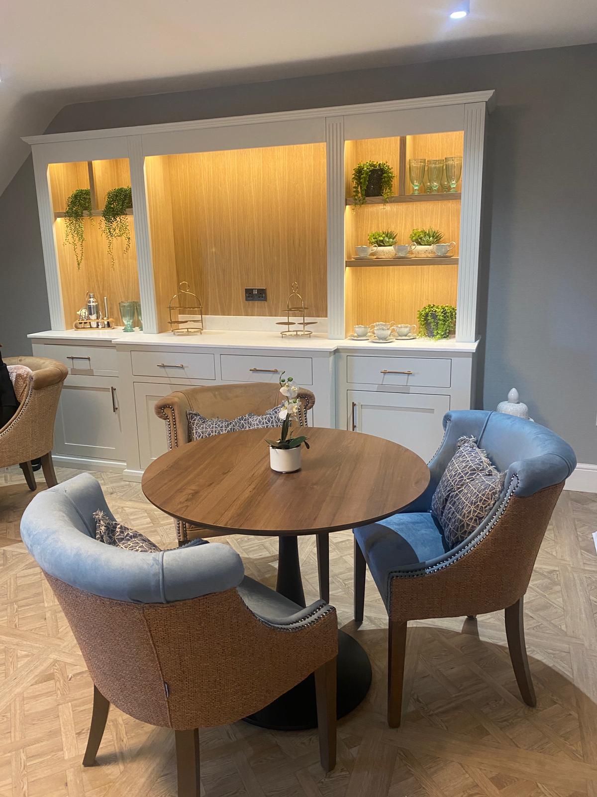 Close-up of the café display unit at Meadowbrook Manor showing illuminated oak shelving with china teacups, glass vases and trailing houseplants